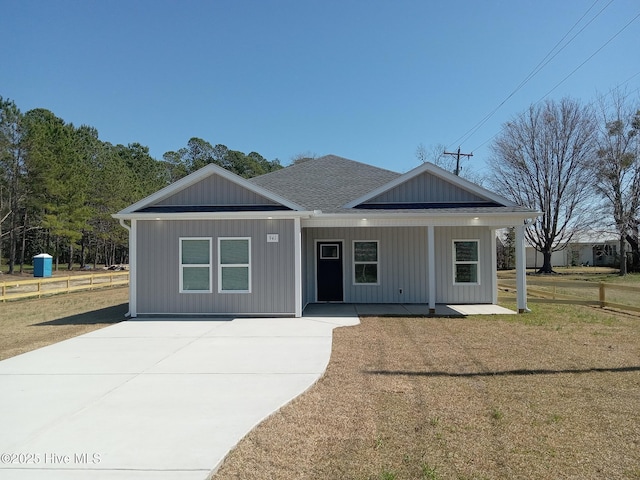 view of front of home with covered porch, a shingled roof, and a front yard