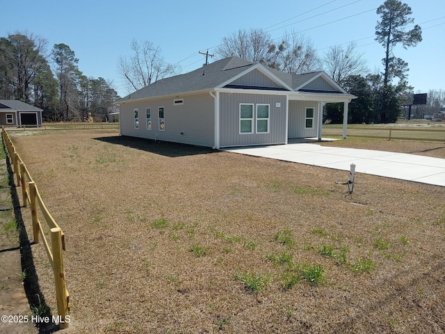 back of property with fence, concrete driveway, roof with shingles, a lawn, and a patio area