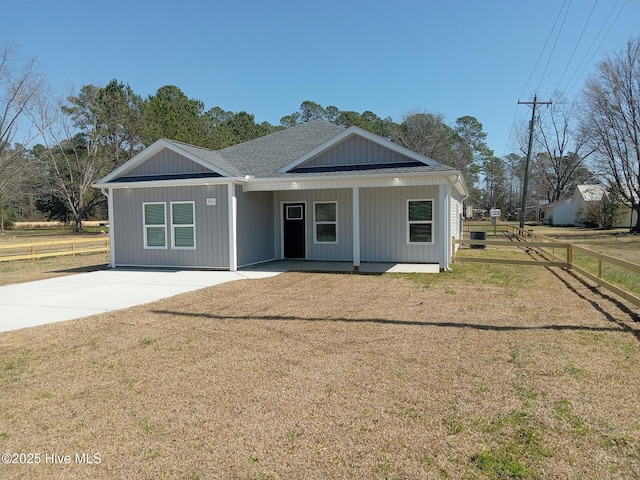 view of front facade with a porch, roof with shingles, a front yard, and fence