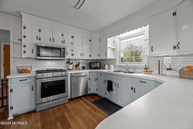 kitchen with appliances with stainless steel finishes, white cabinetry, dark wood-type flooring, tasteful backsplash, and sink