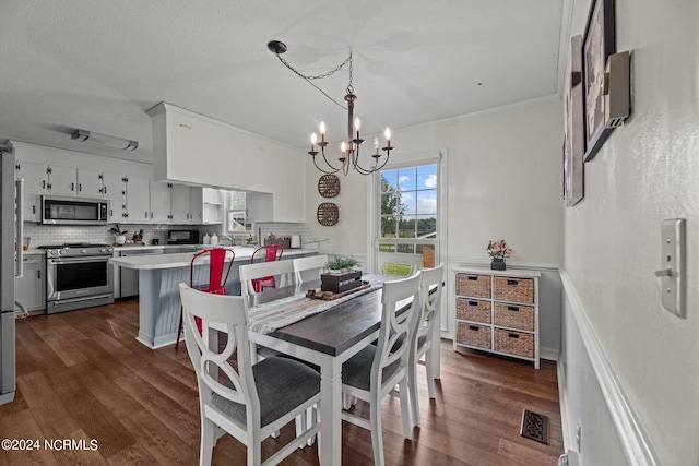 dining space with an inviting chandelier, a textured ceiling, dark wood-type flooring, and crown molding