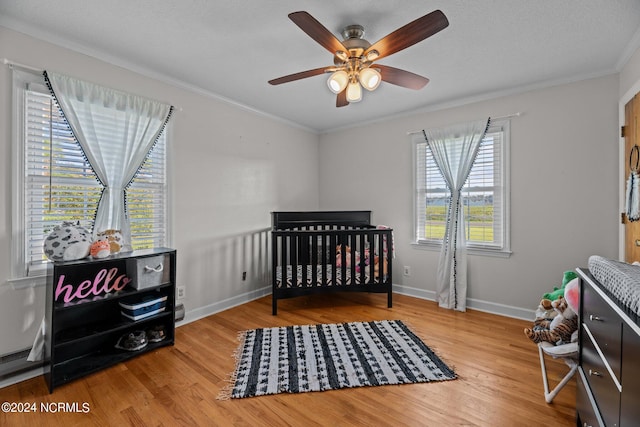 bedroom with a crib, crown molding, ceiling fan, and hardwood / wood-style flooring