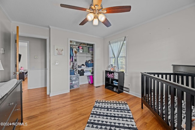 bedroom with a closet, light wood-type flooring, ceiling fan, a crib, and ornamental molding