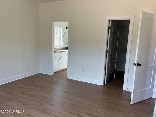 unfurnished bedroom with dark hardwood / wood-style floors, ensuite bathroom, and a walk in closet