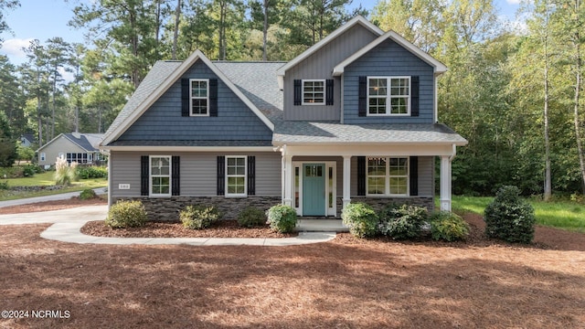 view of front facade with a porch, stone siding, and a shingled roof