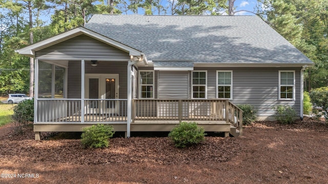 rear view of house featuring a wooden deck, a sunroom, and a shingled roof