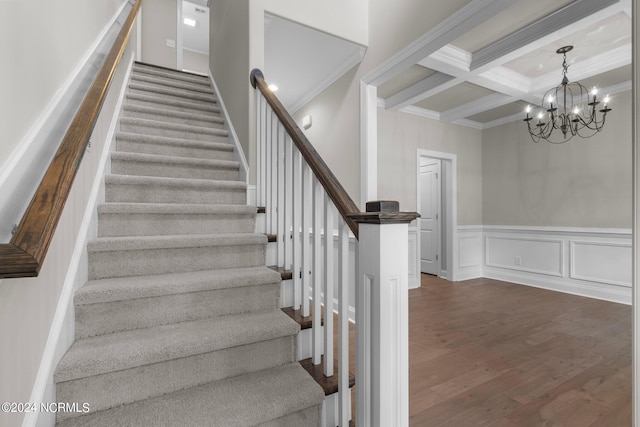 staircase with beamed ceiling, wood finished floors, ornamental molding, and an inviting chandelier
