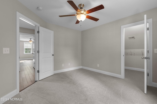 unfurnished bedroom featuring a ceiling fan, a walk in closet, baseboards, carpet flooring, and visible vents