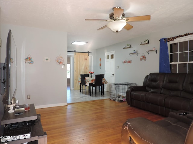 living room with wood-type flooring, ceiling fan, and a barn door