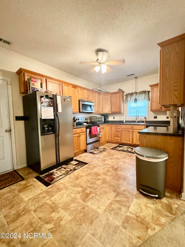 kitchen featuring ceiling fan, hanging light fixtures, sink, a textured ceiling, and stainless steel appliances