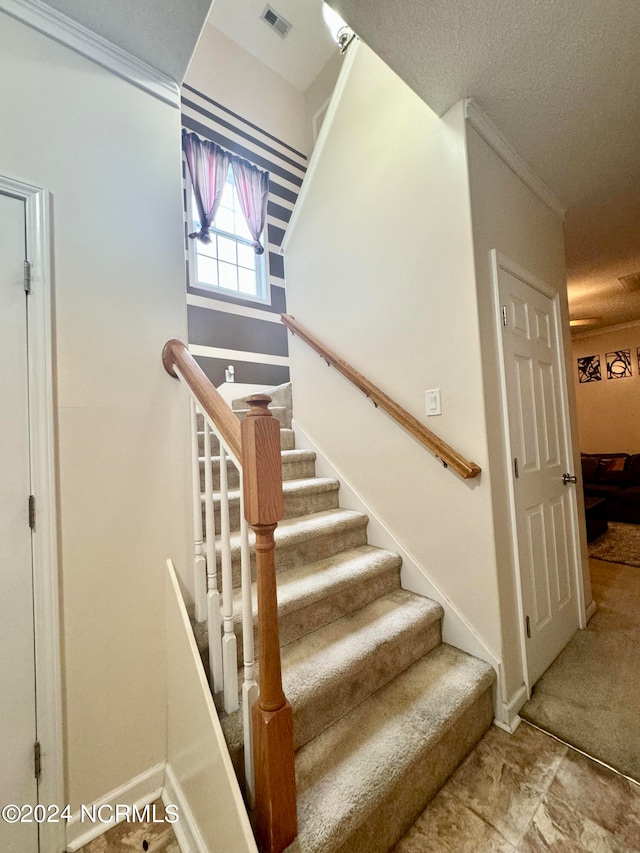 staircase featuring a textured ceiling and crown molding