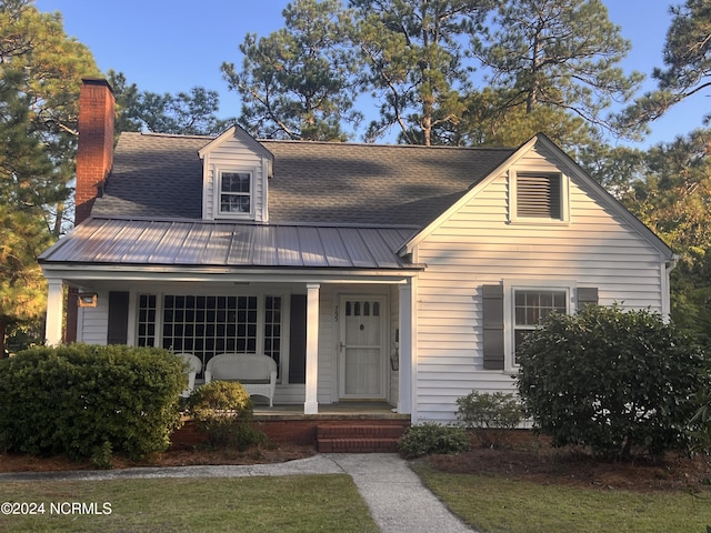 view of front facade featuring roof with shingles, a porch, a chimney, and metal roof
