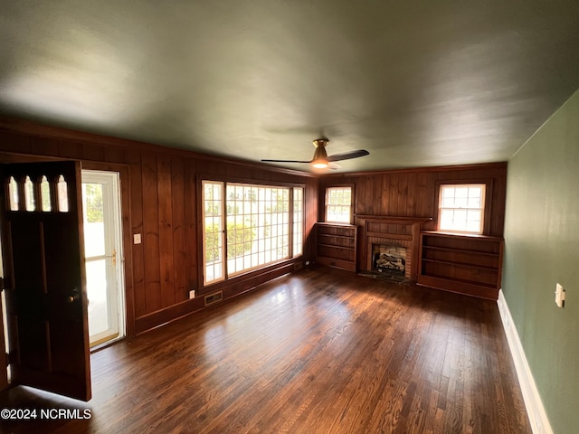 unfurnished living room with wood walls, baseboards, ceiling fan, and dark wood finished floors