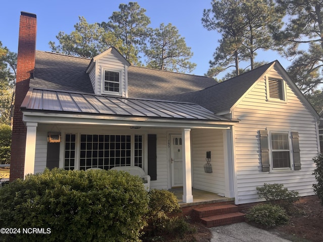 new england style home featuring a standing seam roof, a chimney, metal roof, covered porch, and a shingled roof