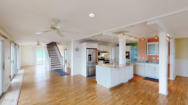 kitchen featuring white cabinets, light wood-type flooring, stainless steel appliances, and an island with sink