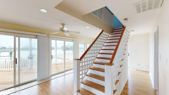 stairs with ceiling fan, hardwood / wood-style floors, and a water view