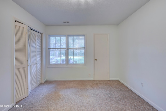 unfurnished bedroom featuring light colored carpet, a textured ceiling, and a closet