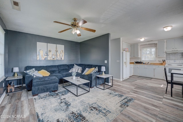 living room with ceiling fan, a textured ceiling, sink, and light hardwood / wood-style floors