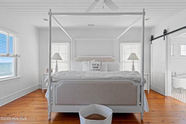 6615 W Beach Dr, Oak Island, NC 28465 - bedroom with light wood-type flooring, a barn door, and ceiling fan