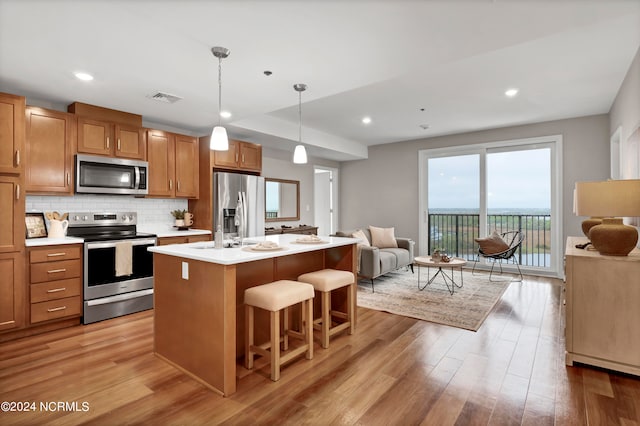 kitchen featuring a breakfast bar, pendant lighting, stainless steel appliances, light wood-type flooring, and a center island with sink