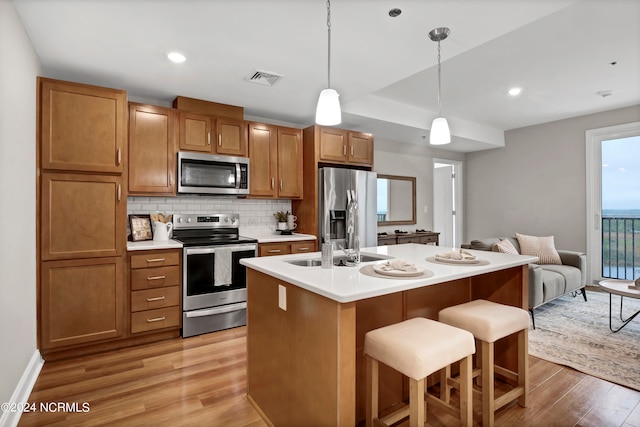 kitchen with light wood-type flooring, a kitchen island with sink, a kitchen bar, hanging light fixtures, and stainless steel appliances