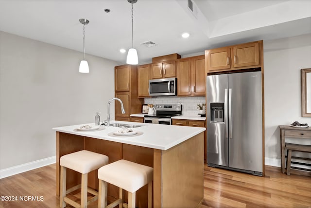 kitchen featuring pendant lighting, an island with sink, sink, appliances with stainless steel finishes, and light hardwood / wood-style floors