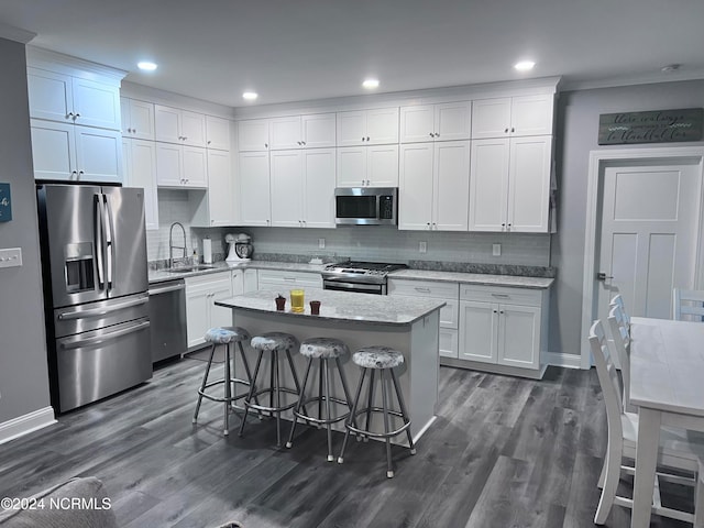 kitchen with appliances with stainless steel finishes, dark wood-type flooring, white cabinets, a breakfast bar area, and sink