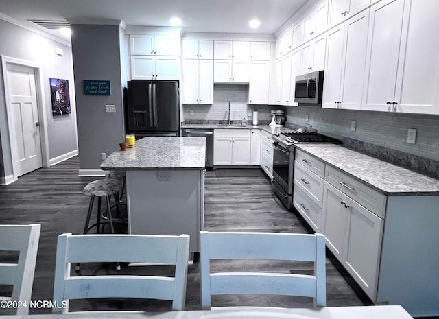 kitchen with light stone counters, a kitchen island, stainless steel appliances, and white cabinets