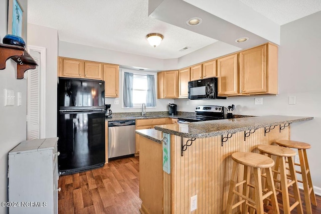 113 Scallop Ln, Carolina Beach, NC 28428 - kitchen featuring black appliances, light brown cabinetry, a peninsula, a textured ceiling, and wood finished floors