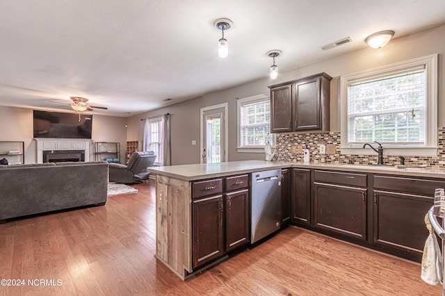 kitchen with dark brown cabinetry, pendant lighting, kitchen peninsula, stainless steel dishwasher, and light hardwood / wood-style flooring