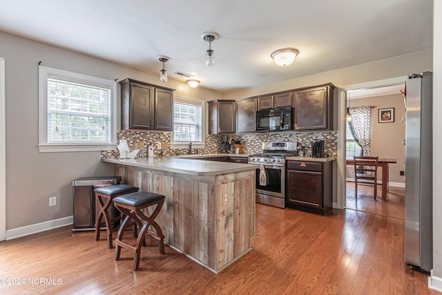 kitchen with hanging light fixtures, kitchen peninsula, stainless steel appliances, a breakfast bar area, and light hardwood / wood-style floors