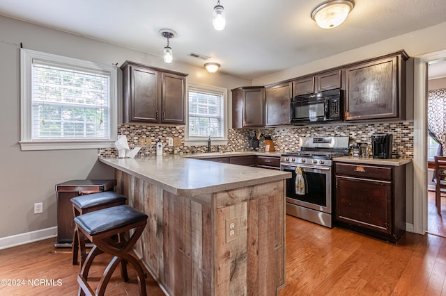 kitchen with pendant lighting, kitchen peninsula, stainless steel gas range, a breakfast bar, and light wood-type flooring