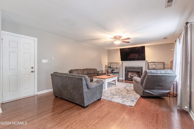 living room with a tile fireplace, wood-type flooring, and ceiling fan