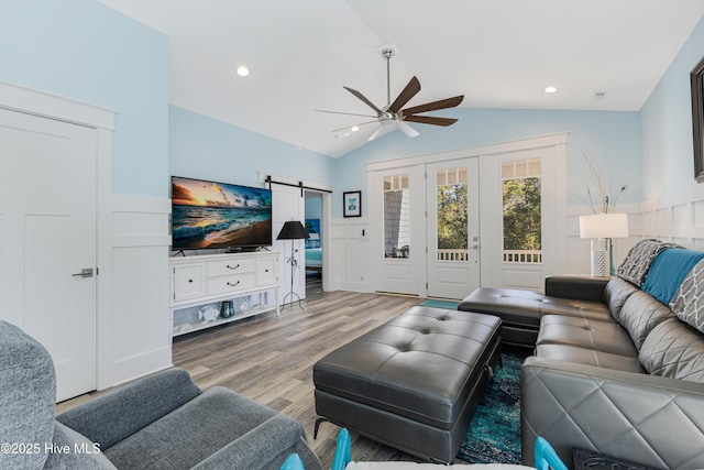 living room featuring a barn door, wood finished floors, wainscoting, ceiling fan, and lofted ceiling