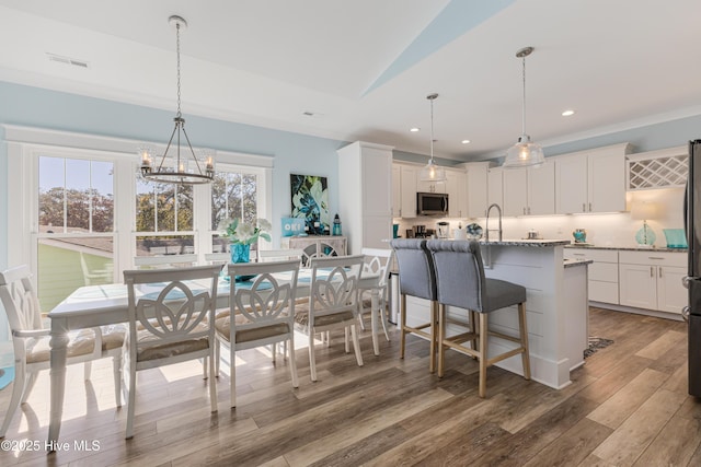 dining room featuring recessed lighting, lofted ceiling, wood finished floors, crown molding, and a notable chandelier