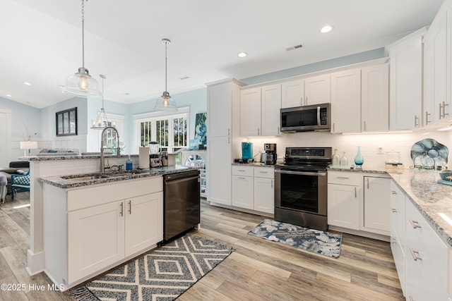 kitchen featuring white cabinets, a sink, light wood-type flooring, tasteful backsplash, and appliances with stainless steel finishes