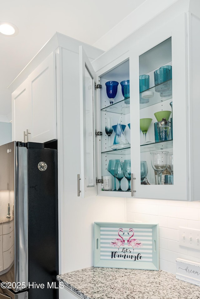 details featuring white cabinets, freestanding refrigerator, and light stone countertops