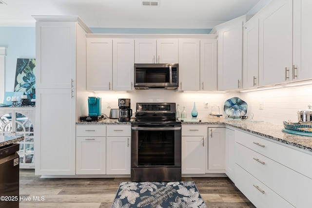 kitchen with light wood finished floors, backsplash, light stone counters, appliances with stainless steel finishes, and white cabinetry