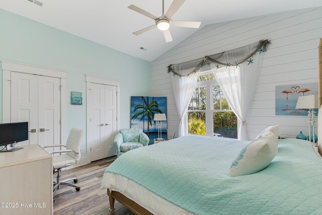 bedroom with wooden walls, wood finished floors, visible vents, two closets, and high vaulted ceiling