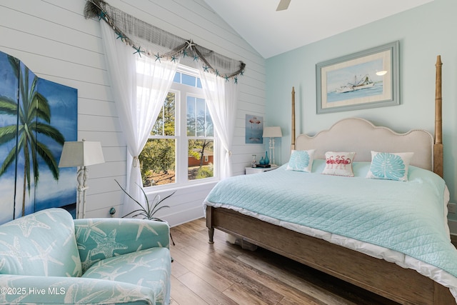bedroom with vaulted ceiling, wood finished floors, wooden walls, and a ceiling fan