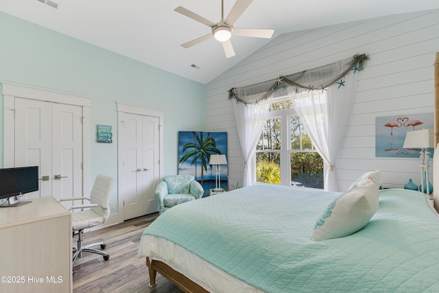 bedroom with a ceiling fan, wood finished floors, lofted ceiling, wood walls, and two closets