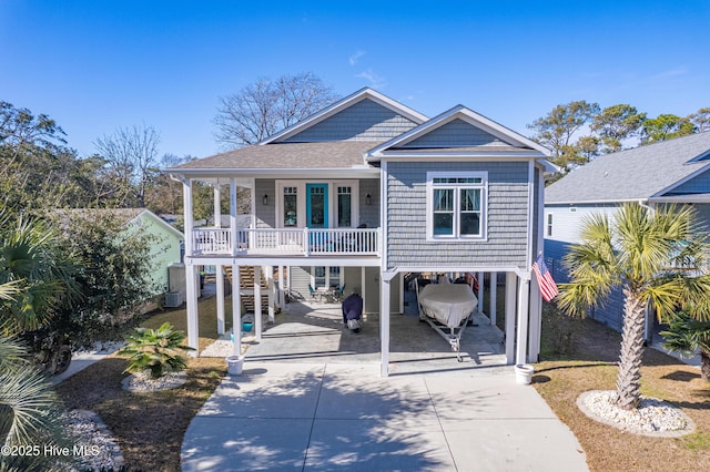 raised beach house with concrete driveway, stairway, a carport, and a shingled roof