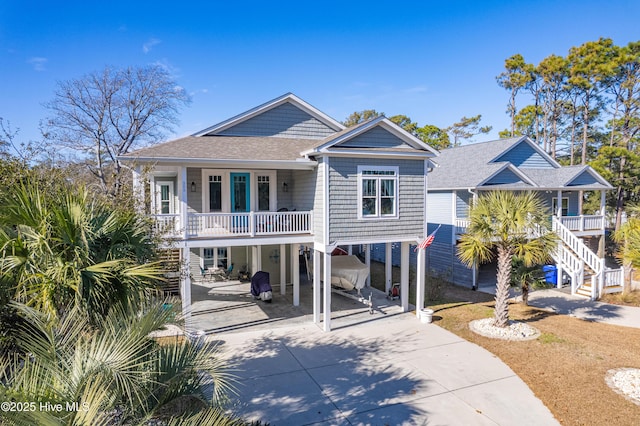 coastal inspired home featuring a carport, stairway, concrete driveway, and a shingled roof