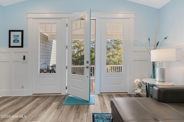 doorway to outside featuring vaulted ceiling, wood finished floors, and a decorative wall