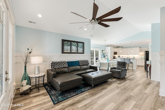 living room with lofted ceiling, a ceiling fan, visible vents, and light wood-style flooring