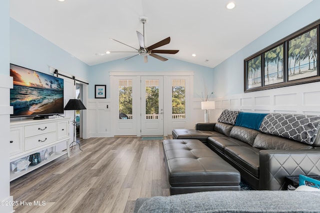 living area with light wood finished floors, a wainscoted wall, a barn door, ceiling fan, and a decorative wall