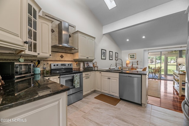 kitchen with vaulted ceiling with skylight, sink, kitchen peninsula, wall chimney exhaust hood, and appliances with stainless steel finishes