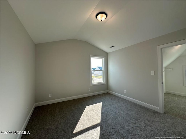 additional living space with dark colored carpet and vaulted ceiling