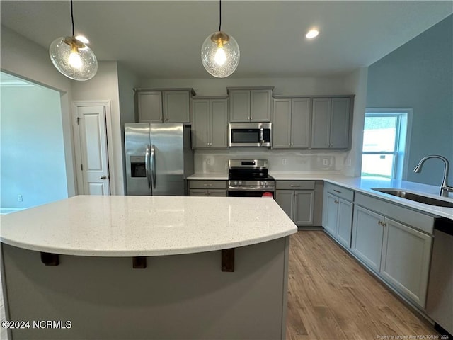 kitchen with sink, a kitchen island, decorative light fixtures, stainless steel appliances, and light wood-type flooring