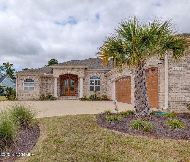 8711 Compass Pointe W Wynd Wynd NE, Leland, NC 28451 - mediterranean / spanish house featuring a shingled roof, brick siding, a garage, concrete driveway, and french doors
